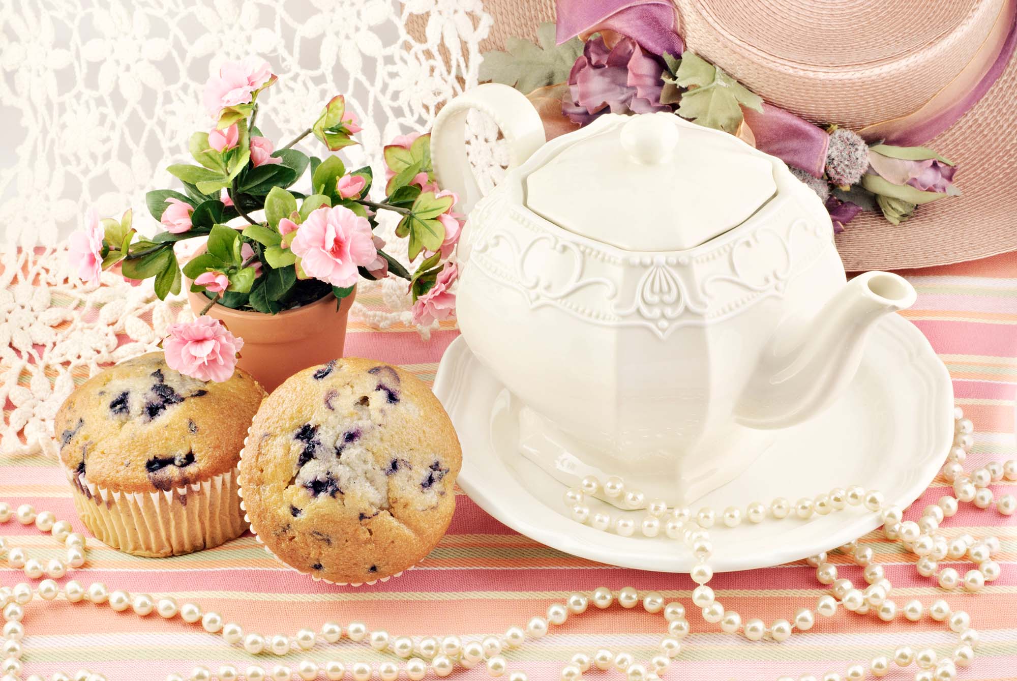 a white tea pot and blueberry muffins on a pink table cloth with flowers and pearls